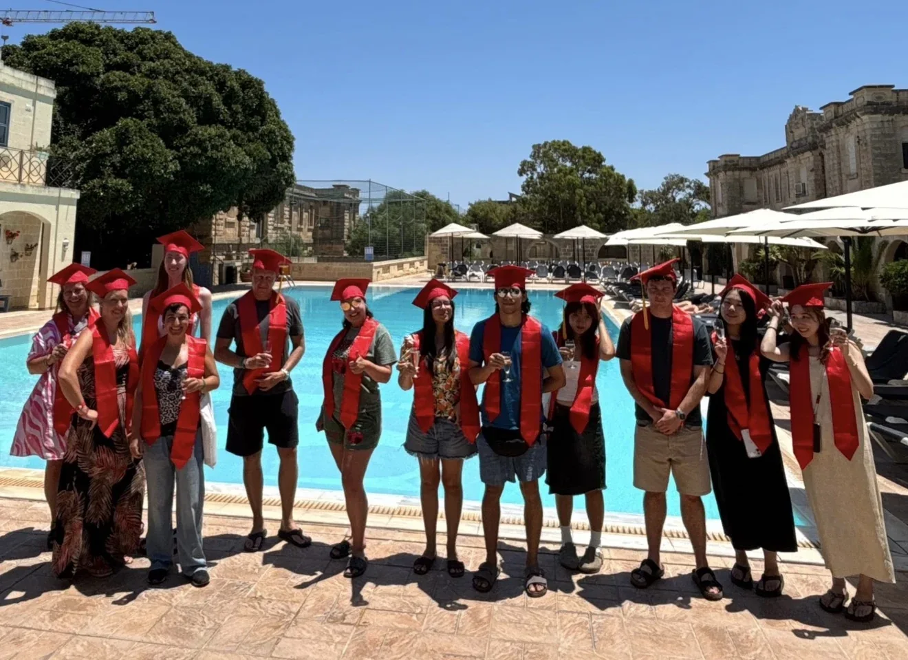 Grupo de estudiantes celebrando su graduación junto a una piscina